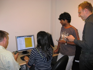 photo of four people using the CoSearch system in which they use mobile phones to simultaenously search on a single shared display